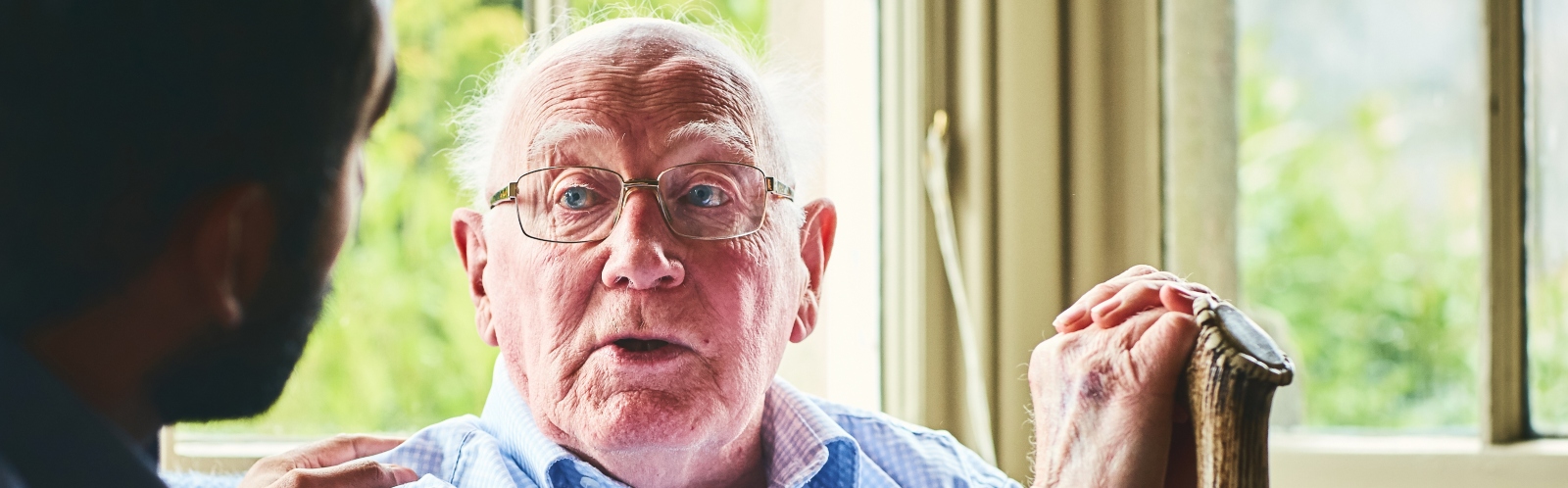 An older man with glasses is comforted by a younger medical professional