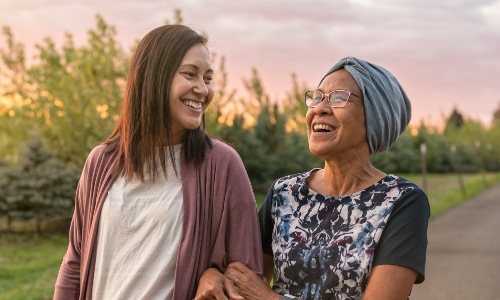 A young woman walking arm-in-arm with her older mother, both smiling