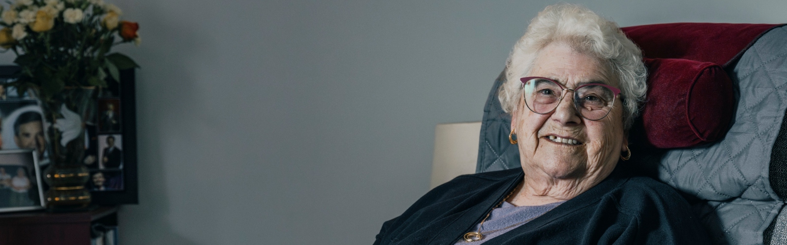 An older woman with white curly hair and glasses smiles at the camera