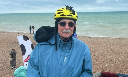 An older man with a grey moustache, dressed in cycling kit at the seaside