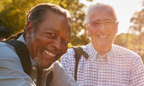 Two older men smile towards the camera, as evening sun shines in the background